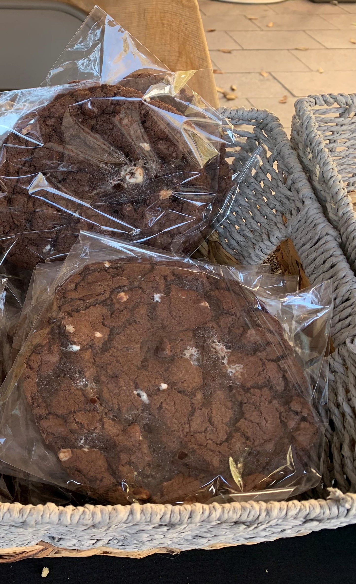 Packaged chocolate chocolate chip cookies with visible white marshmallows, presented in a woven basket.