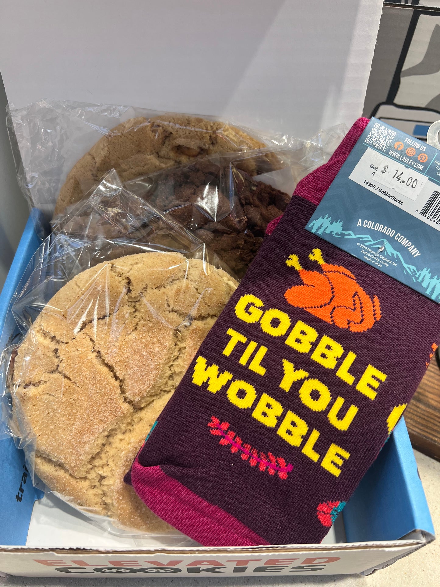 Cookies in a box with a Thanksgiving sock labeled 'Gobble Til You Wobble' on top.