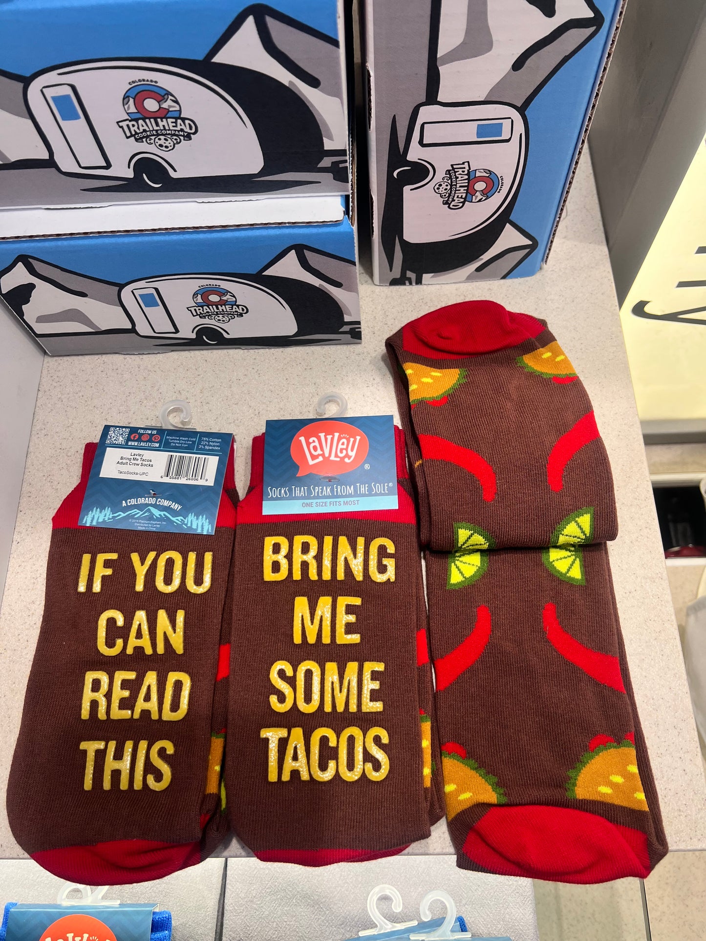 Pair of socks with taco design and text 'if you can read this bring me tacos" on a white surface.