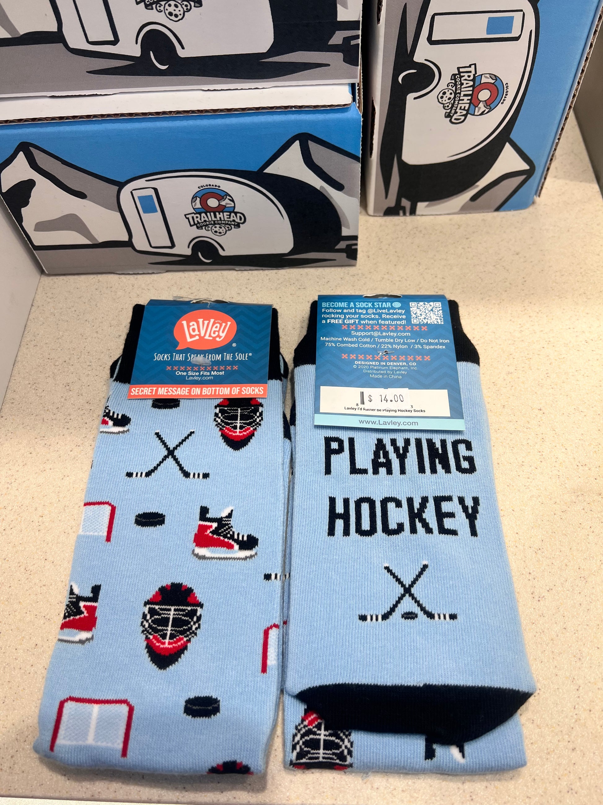 Hockey-themed blue socks with phrase I'd rather be playing hockey with packaging on a beige surface