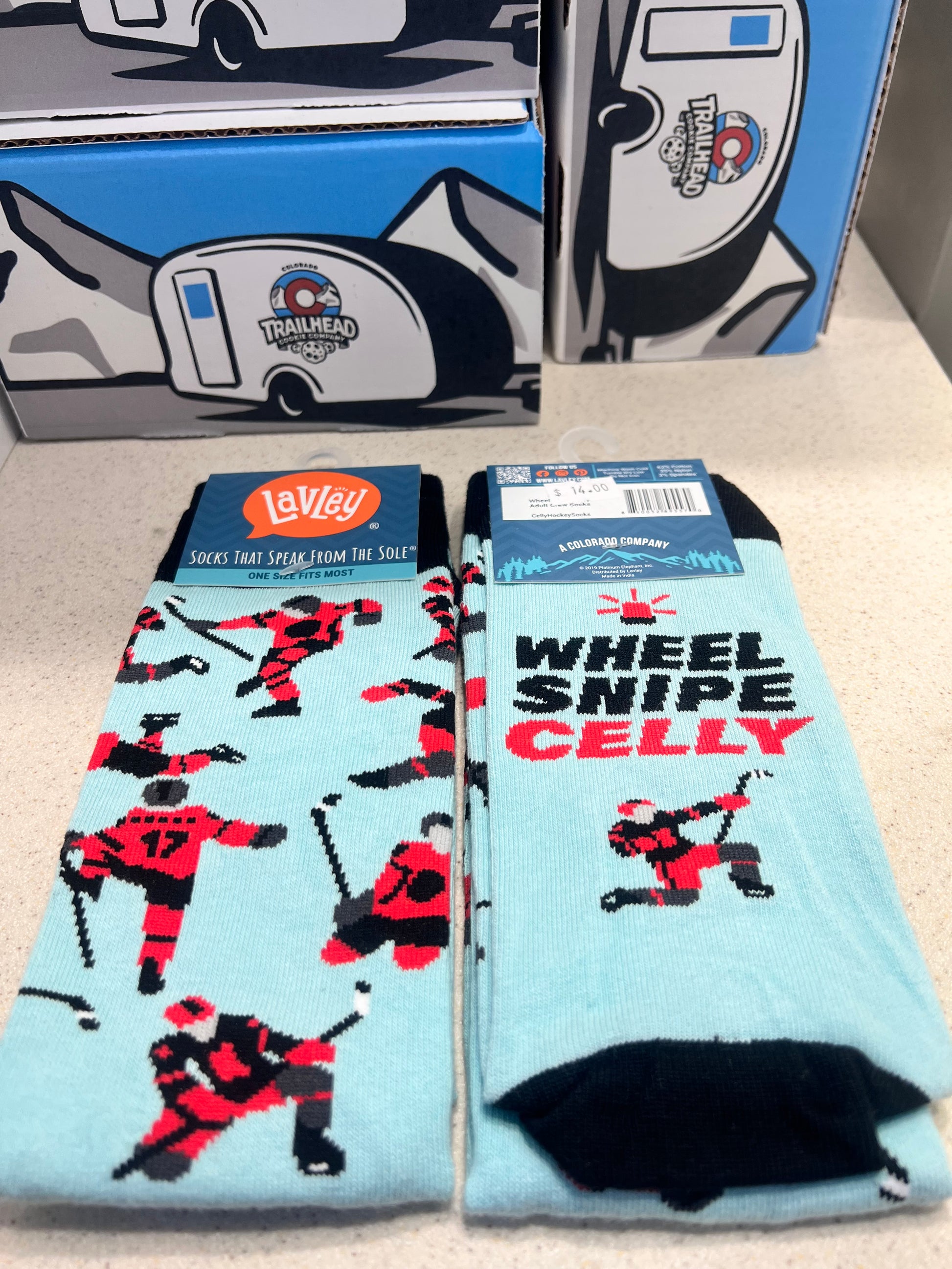 Light blue socks with red and black hockey graphics 'wheel snipe celly' displayed on a beige surface