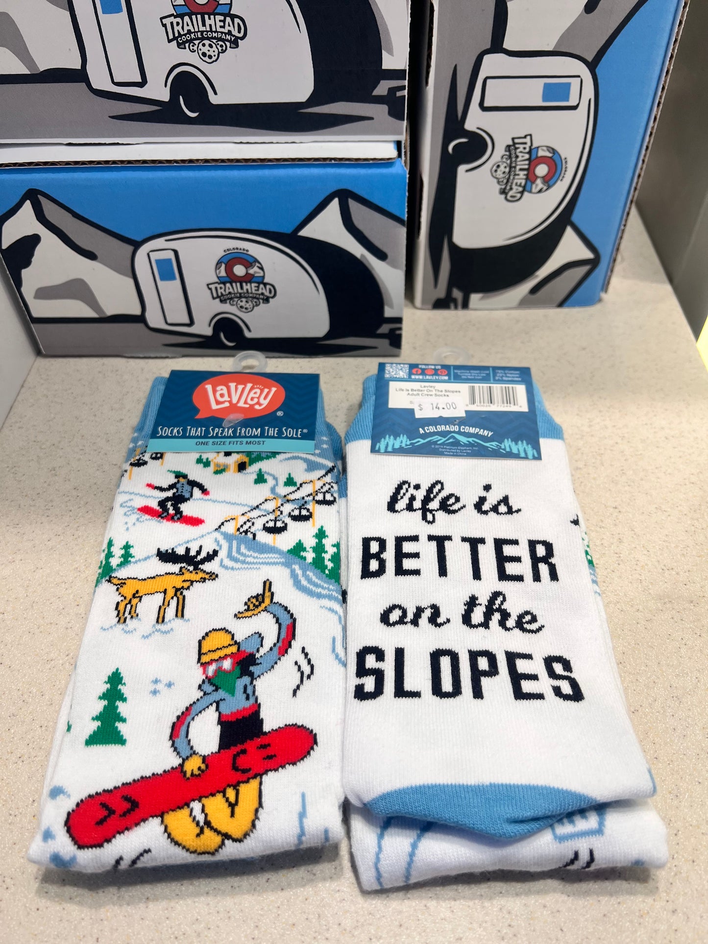 Socks with 'life is better on the slopes' text and cartoon design, displayed with packaging.