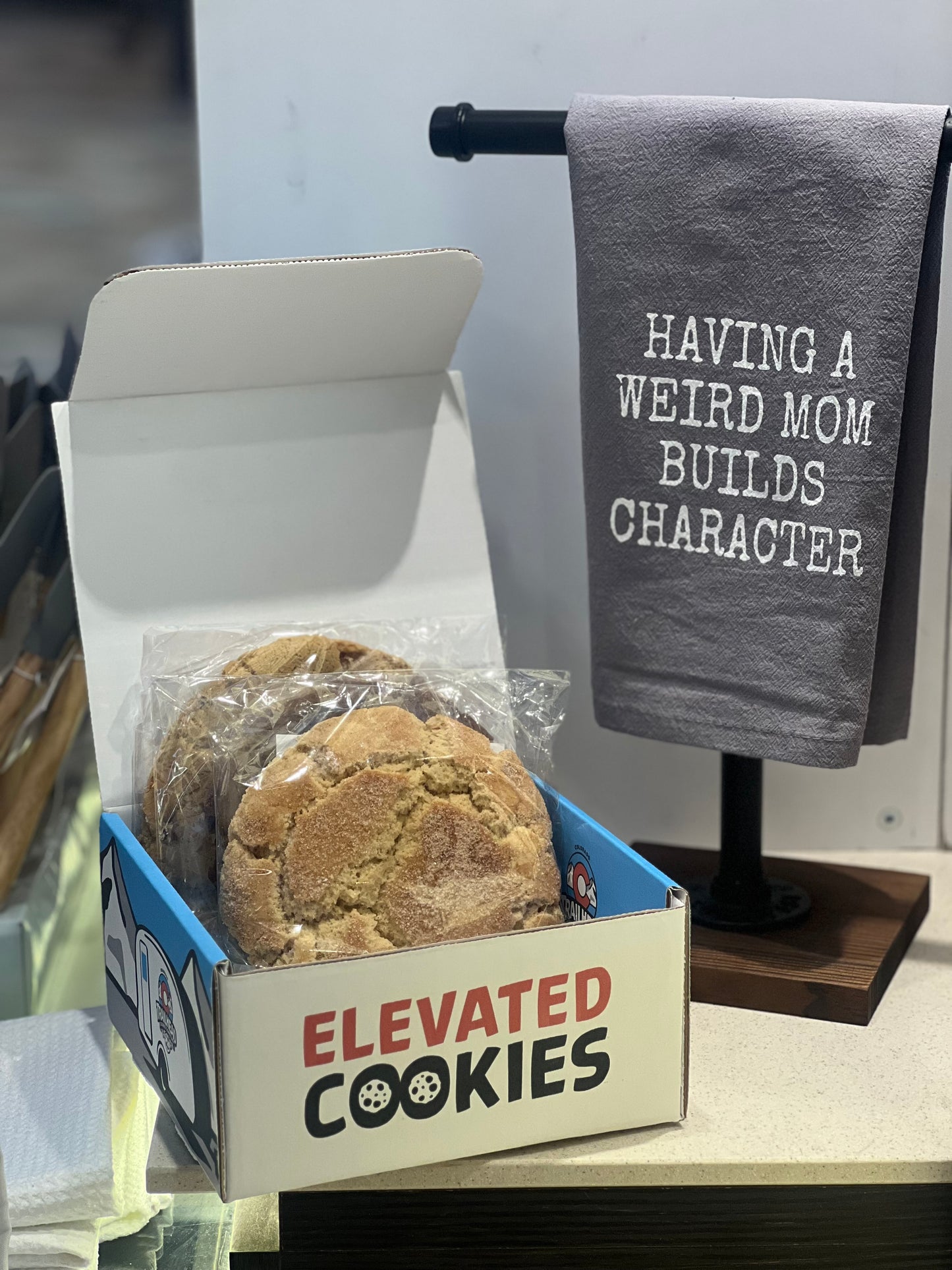Box of cookies with 'Elevated Cookies' branding next to a towel with text on a stand.