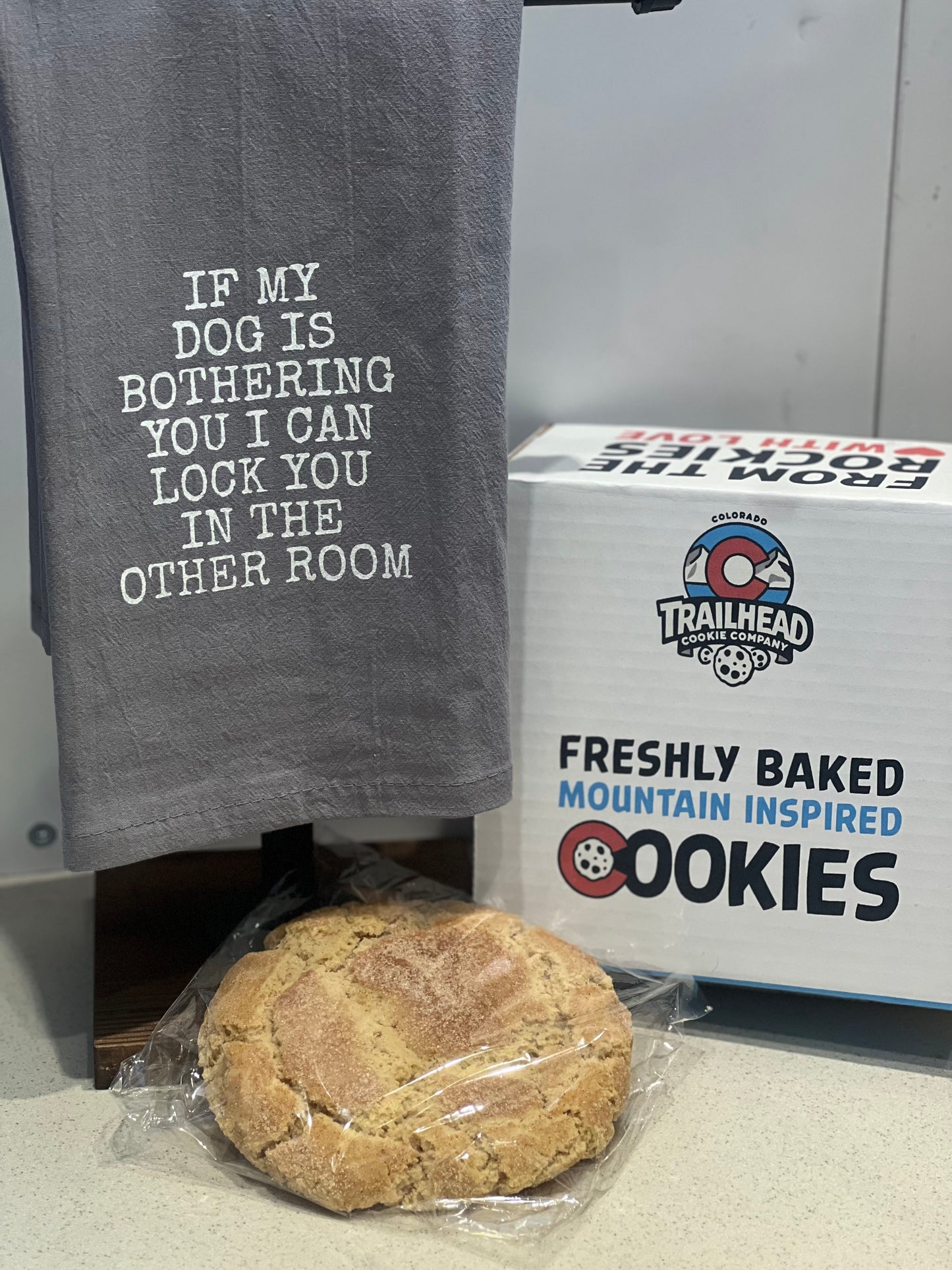 Gray towel with humorous text, a cookie, and a box of cookies on a surface.