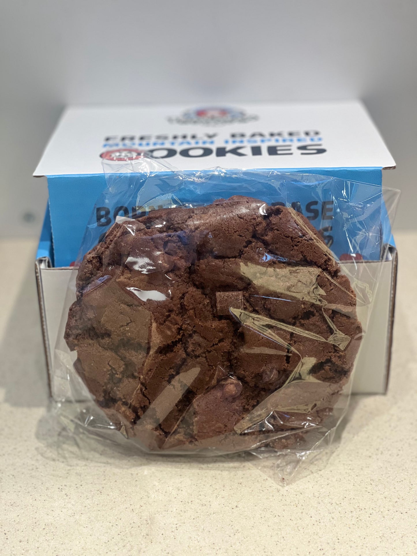Chocolate cookie in a clear plastic bag with a branded box in the background.