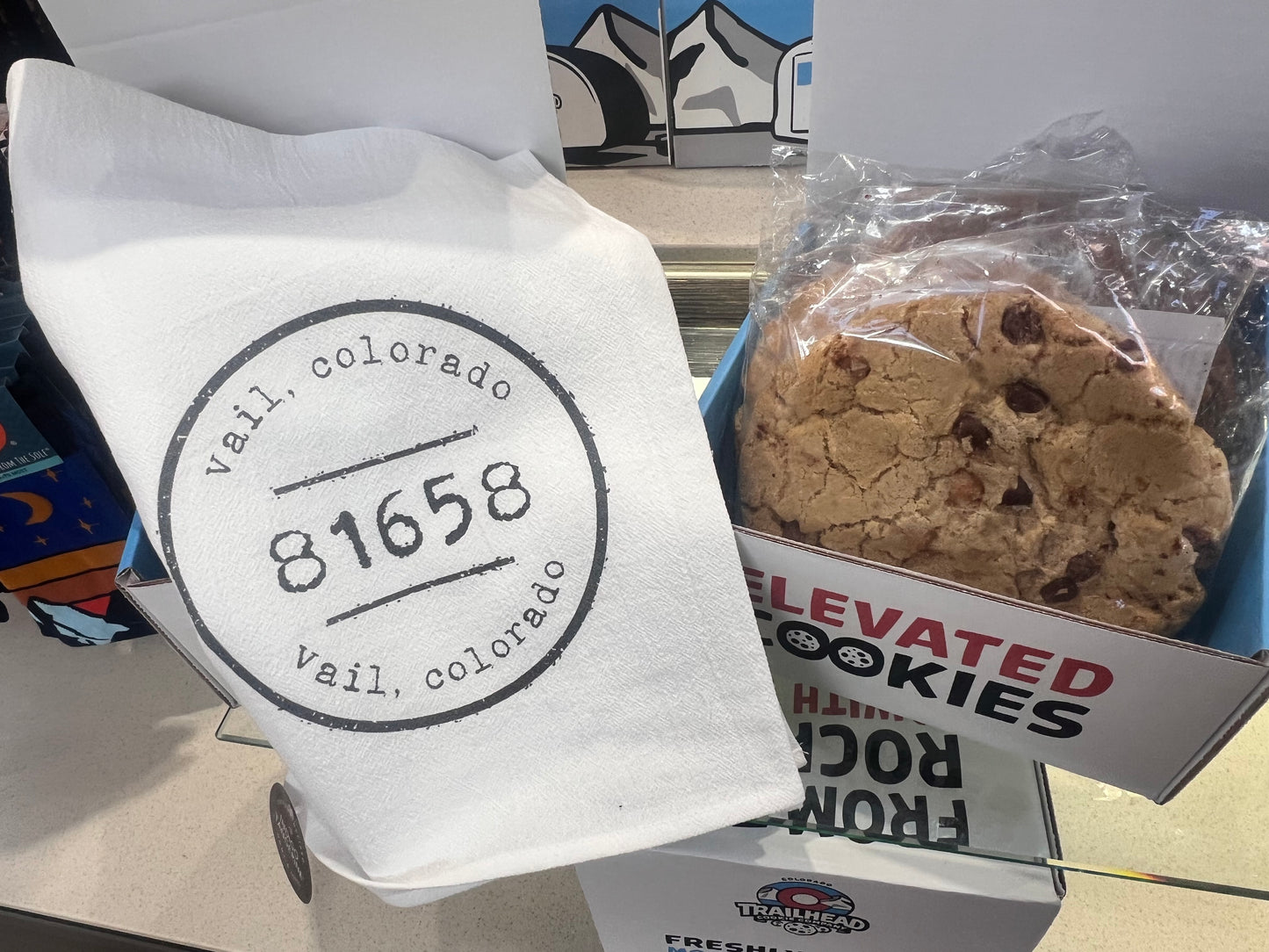 Packaged cookies with a 'Vail, Colorado' stamp on a white towel, displayed in front of a 'Elevated Cookies' sign.